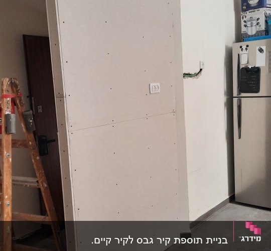 קיר גבס מותקן עם שקע חשמל ולידו סולם
